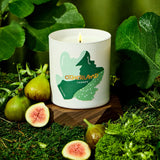 Candle with 'Otherland' branding surrounded by figs and greenery