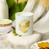 Candle with a Otherland logo on a table with cookies and greenery