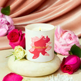 Candle with a decorative label surrounded by pink and white roses on a soft pink fabric background