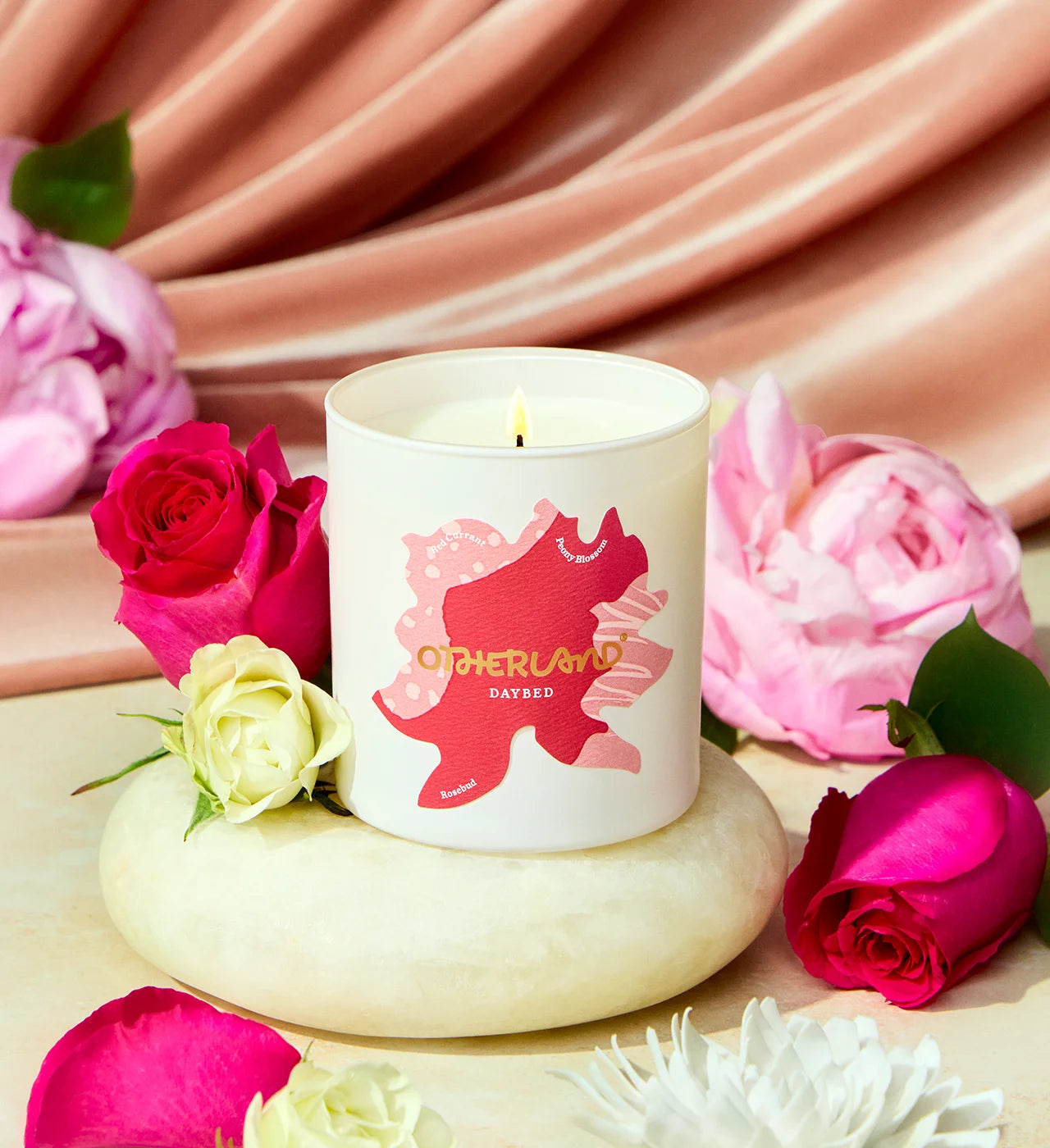Candle with a decorative label surrounded by pink and white roses on a soft pink fabric background - View 2