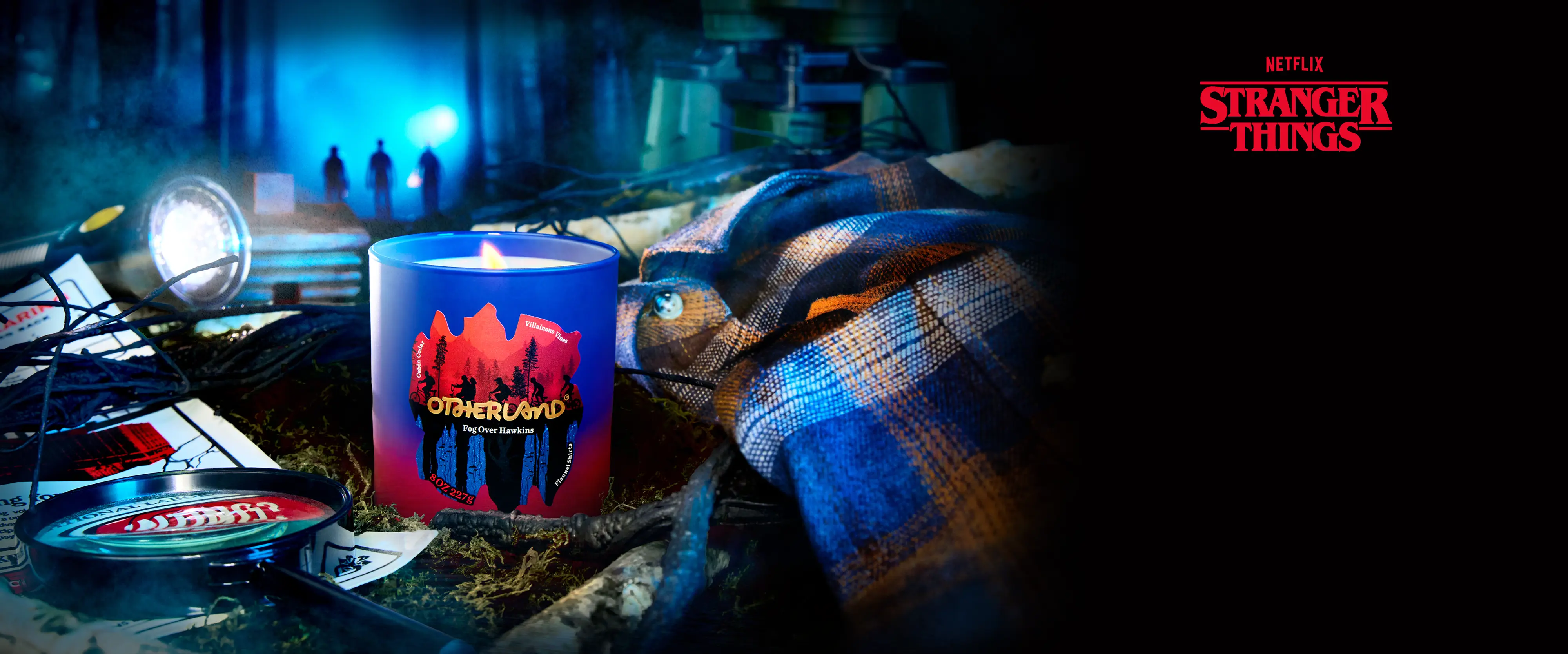 Candle with 'Stranger Things' logo on a table with props and 'Stranger Things' logo in the corner.