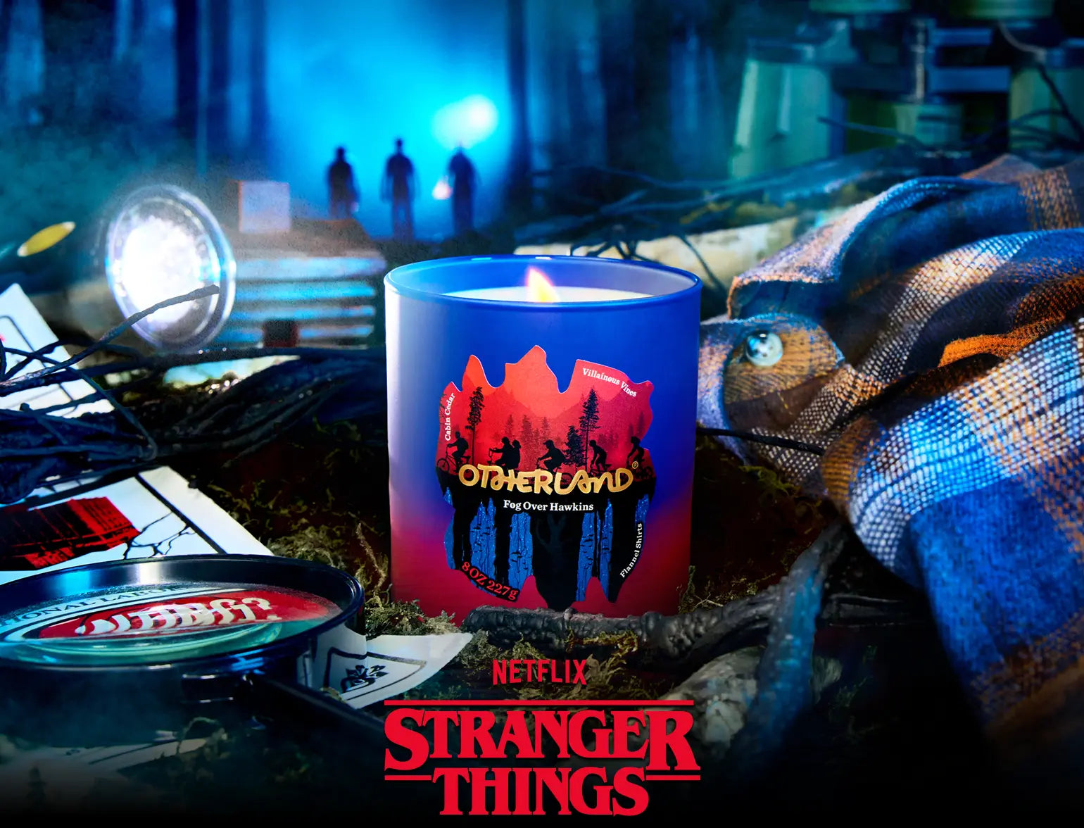 Candle with 'Stranger Things' design on a table with show props and logo.