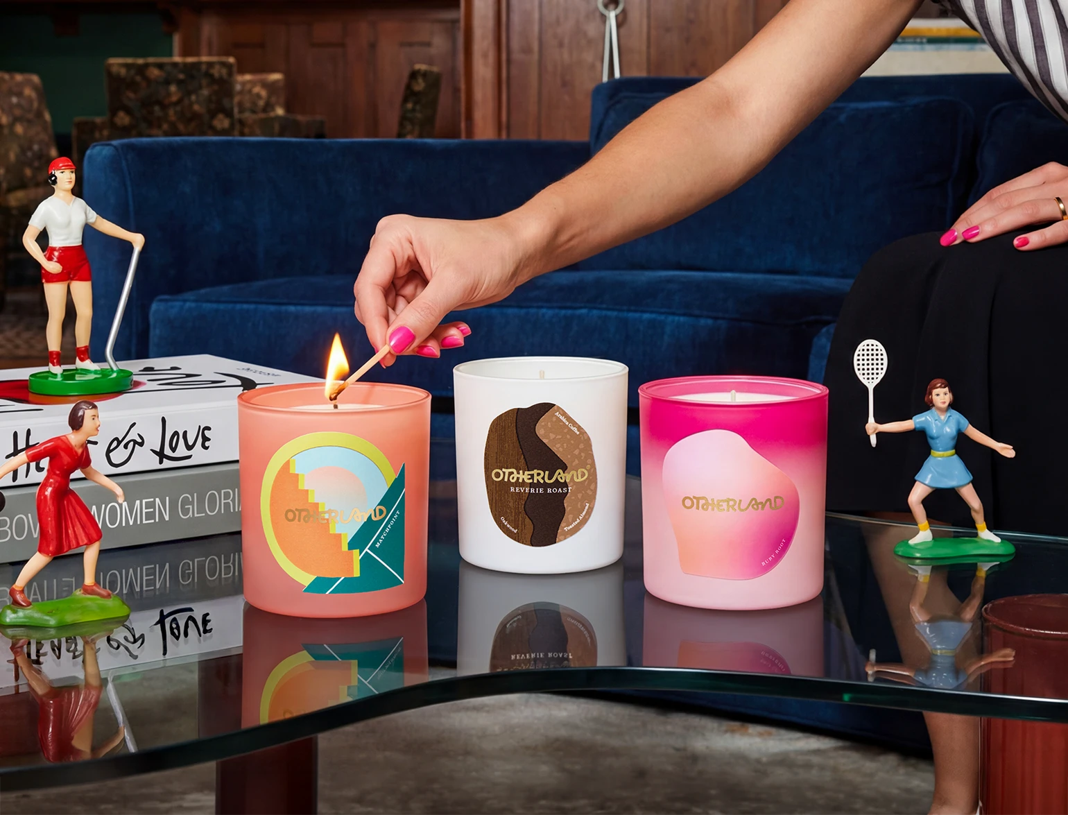 Person lighting a candle with decorative candles and small figures on a table.