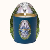 Candle in a blue container with mountain design and 'Otherland' branding, surrounded by nature-themed elements.