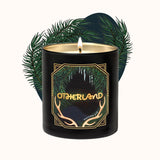 Black candle with gold design and 'Otherland' branding, surrounded by green leaves on a white background