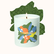 Candle with colorful leaf design and 'Otherland' branding on a white background