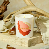 Candle with 'Otherland' branding on a natural setting with driftwood and shells.
