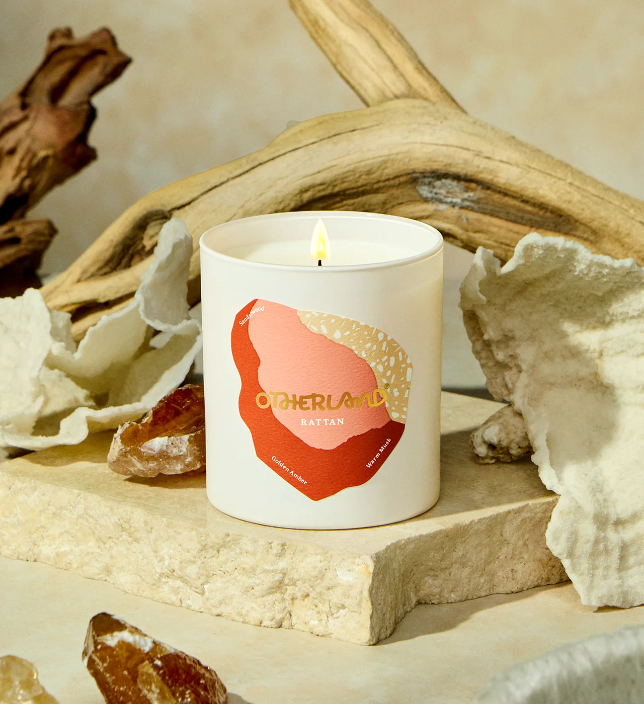 Candle with 'Otherland' branding on a natural setting with driftwood and shells. - View 2