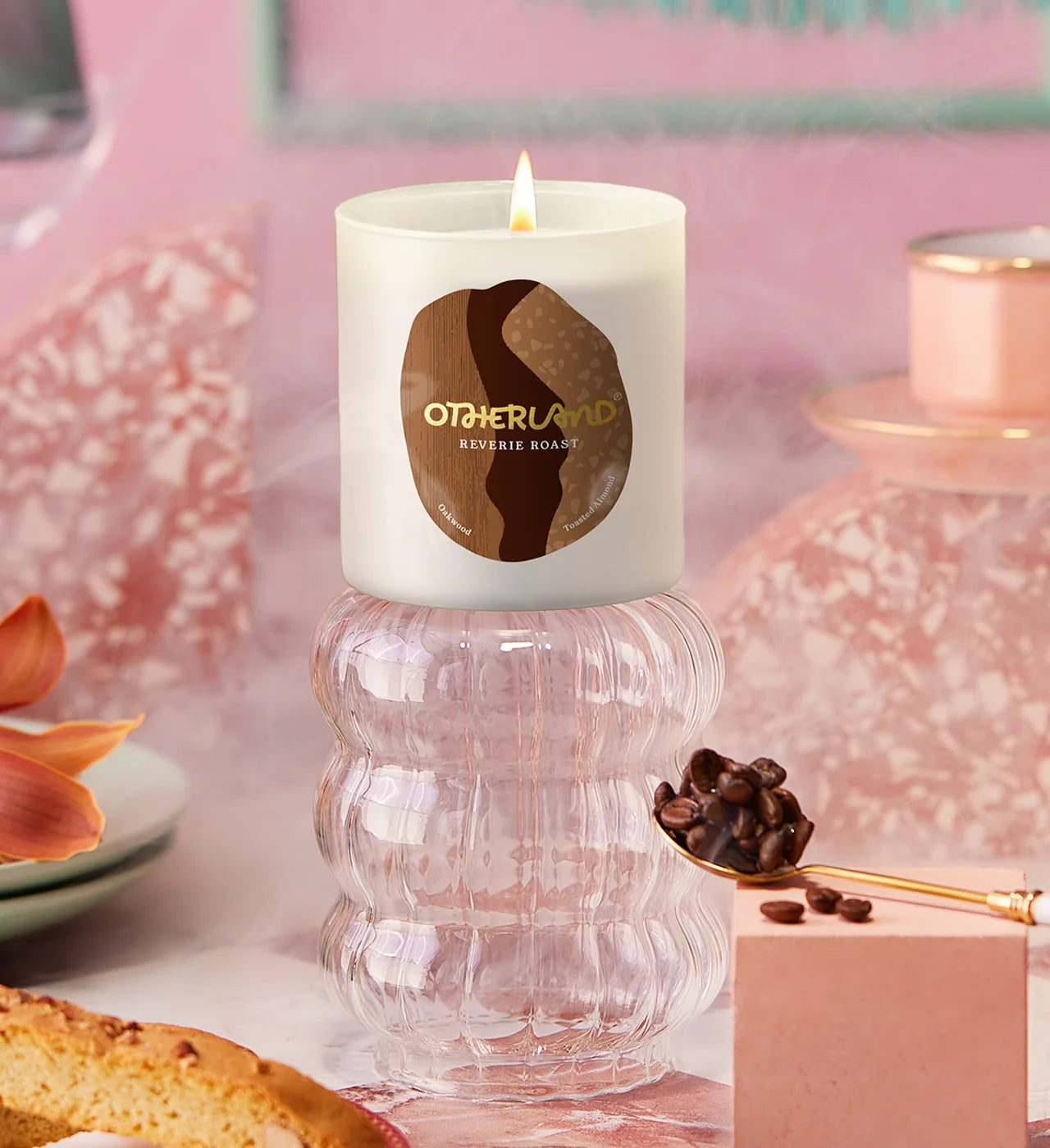 Candle with Otherland on a decorative surface with coffee beans and pastries. - View 2