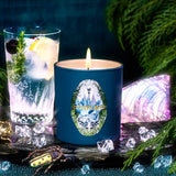 Blue candle with a decorative label next to a glass of water and ice, with a dark background and decorative elements.
