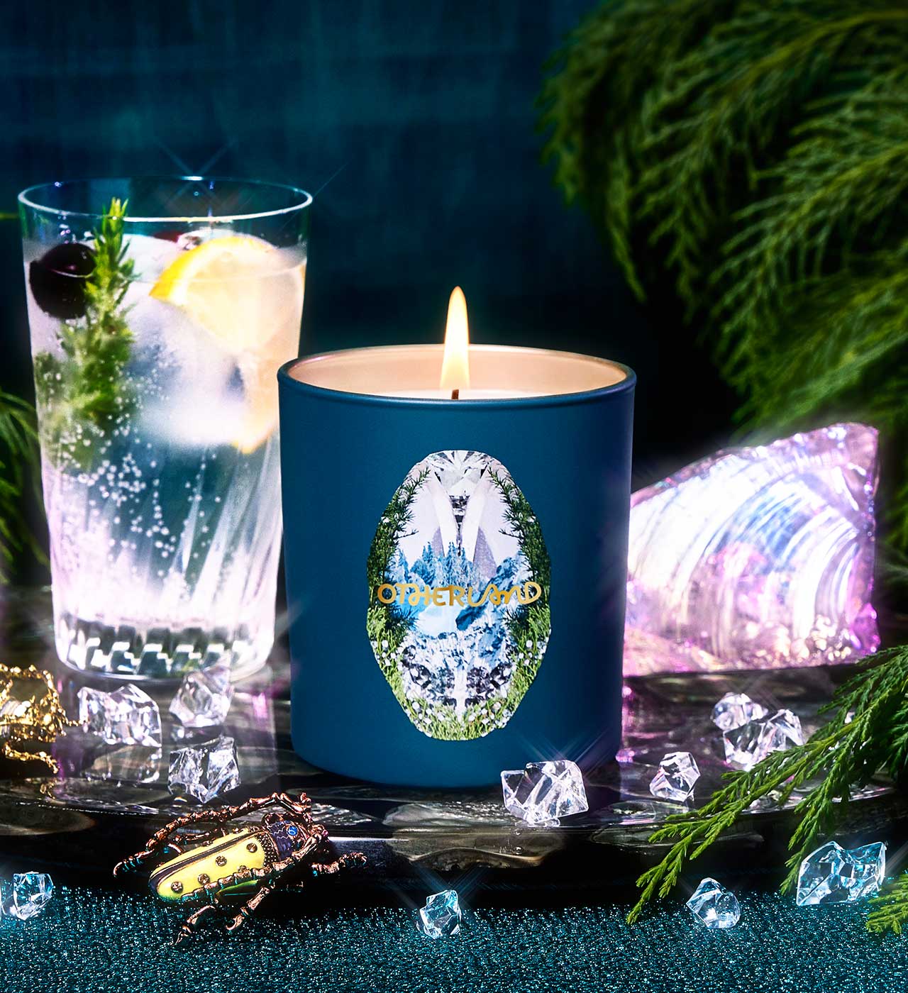 Blue candle with a decorative label next to a glass of water and ice, with a dark background and decorative elements. - View 2