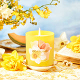 Yellow candle with floral design on a table with yellow flowers and a blue sky background