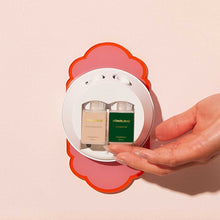 Hand holding a Pura diffuser kit with two refills inside against a light pink background