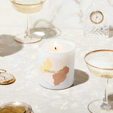 Candle with 'Otherland' branding on a table with glasses and coins