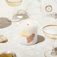 Candle with 'Otherland' branding on a table with glasses and coins