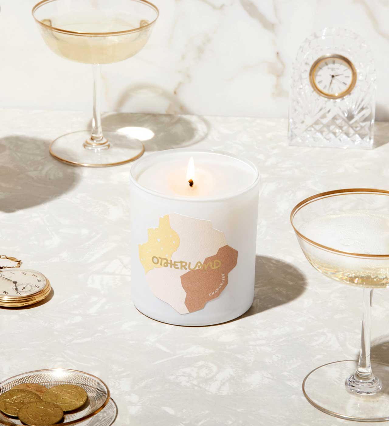 Candle with 'Otherland' branding on a table with glasses and coins - View 2