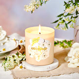 Candle with a floral design on a marble coaster surrounded by flowers and tea cups.