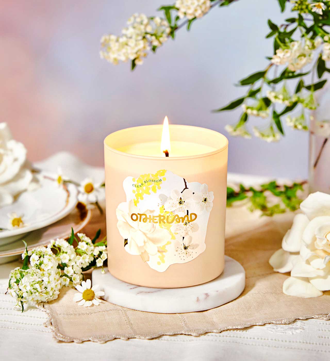 Candle with a floral design on a marble coaster surrounded by flowers and tea cups. - View 2
