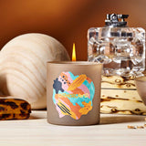 Candle with colorful design and 'Otherland' branding on a wooden surface.