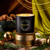 Black candle with 'Otherland' branding on a decorative surface with greenery and gold accents.