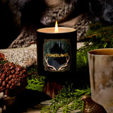 Candle with 'Otherland' branding in a natural setting with greenery and a log.