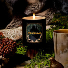 Candle with 'Otherland' branding in a natural setting with greenery and a log.