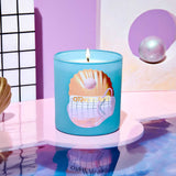 Blue candle with a shell design on a reflective surface with a pink and white background