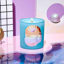 Blue candle with a shell design on a reflective surface with a pink and white background