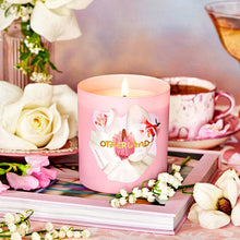 Pink candle with floral design on a table with flowers and a teacup.