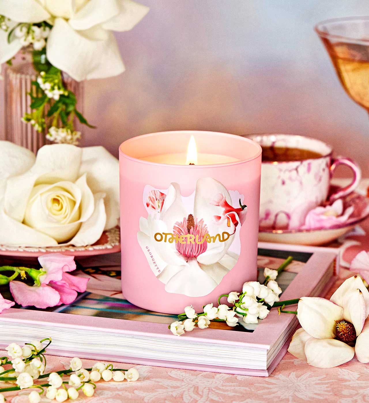 Pink candle with floral design on a table with flowers and a teacup. - View 2