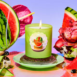Green candle with watermelon design on a colorful background with watermelon slices and flowers.