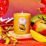 Yellow candle with a mango label on a decorative surface with fruits and flowers