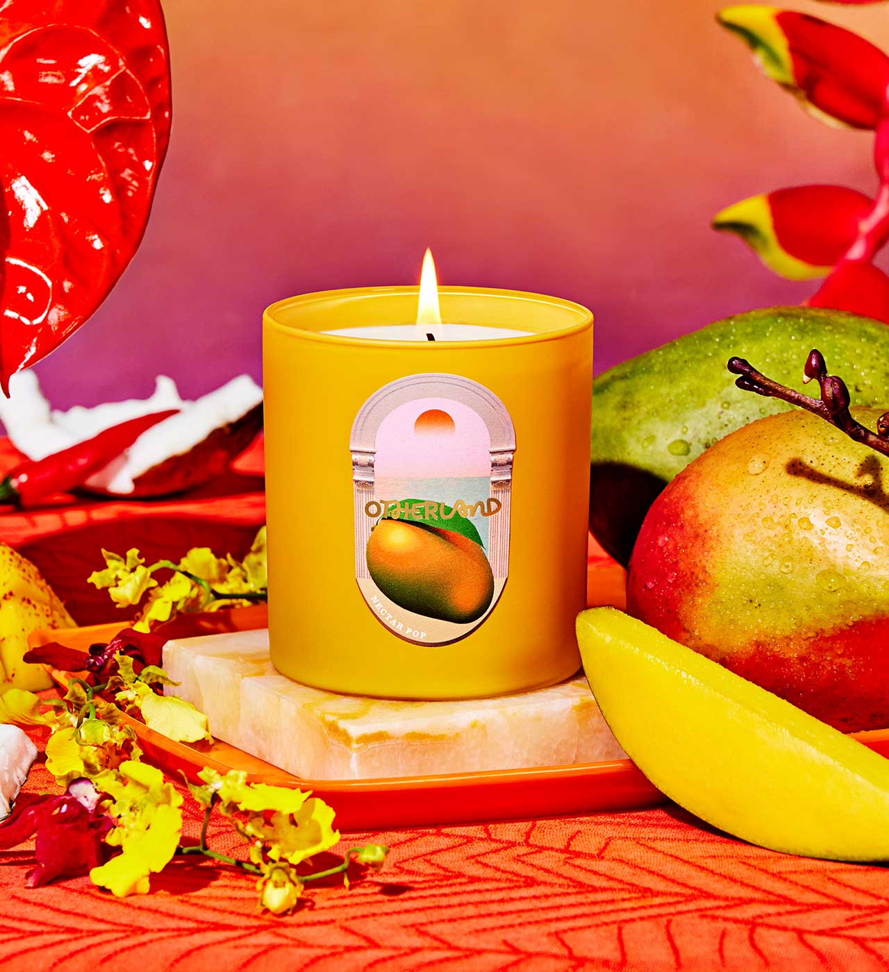 Yellow candle with a mango label on a decorative surface with fruits and flowers - View 2