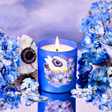 Blue candle with floral design surrounded by blue flowers on a reflective surface