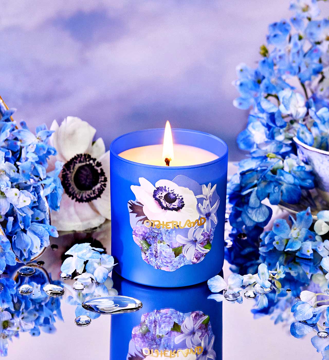 Blue candle with floral design surrounded by blue flowers on a reflective surface - View 2