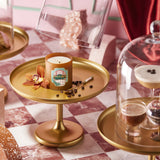 Candle on a gold tray with decorative elements on a checkered tablecloth