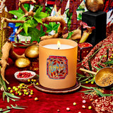Decorative candle with intricate design on a red surface with plants and small objects.