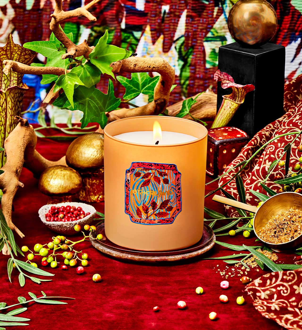 Decorative candle with intricate design on a red surface with plants and small objects. - View 2