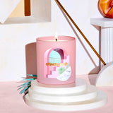 Pink candle with a decorative label on a white pedestal against a light pink background