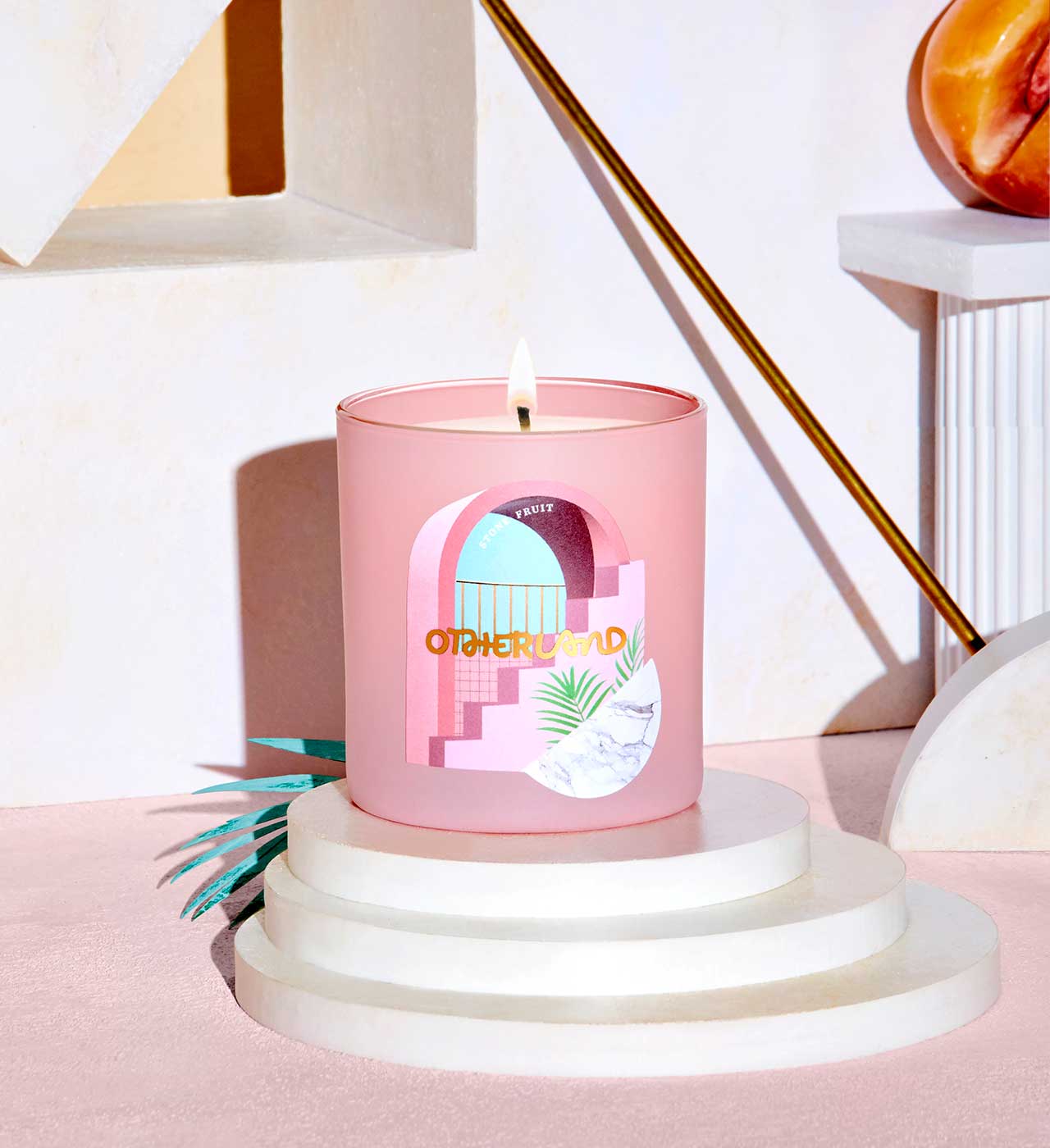 Pink candle with a decorative label on a white pedestal against a light pink background - View 2