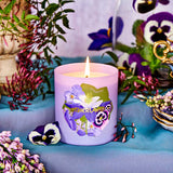 Purple candle with floral design on a table with flowers and plants