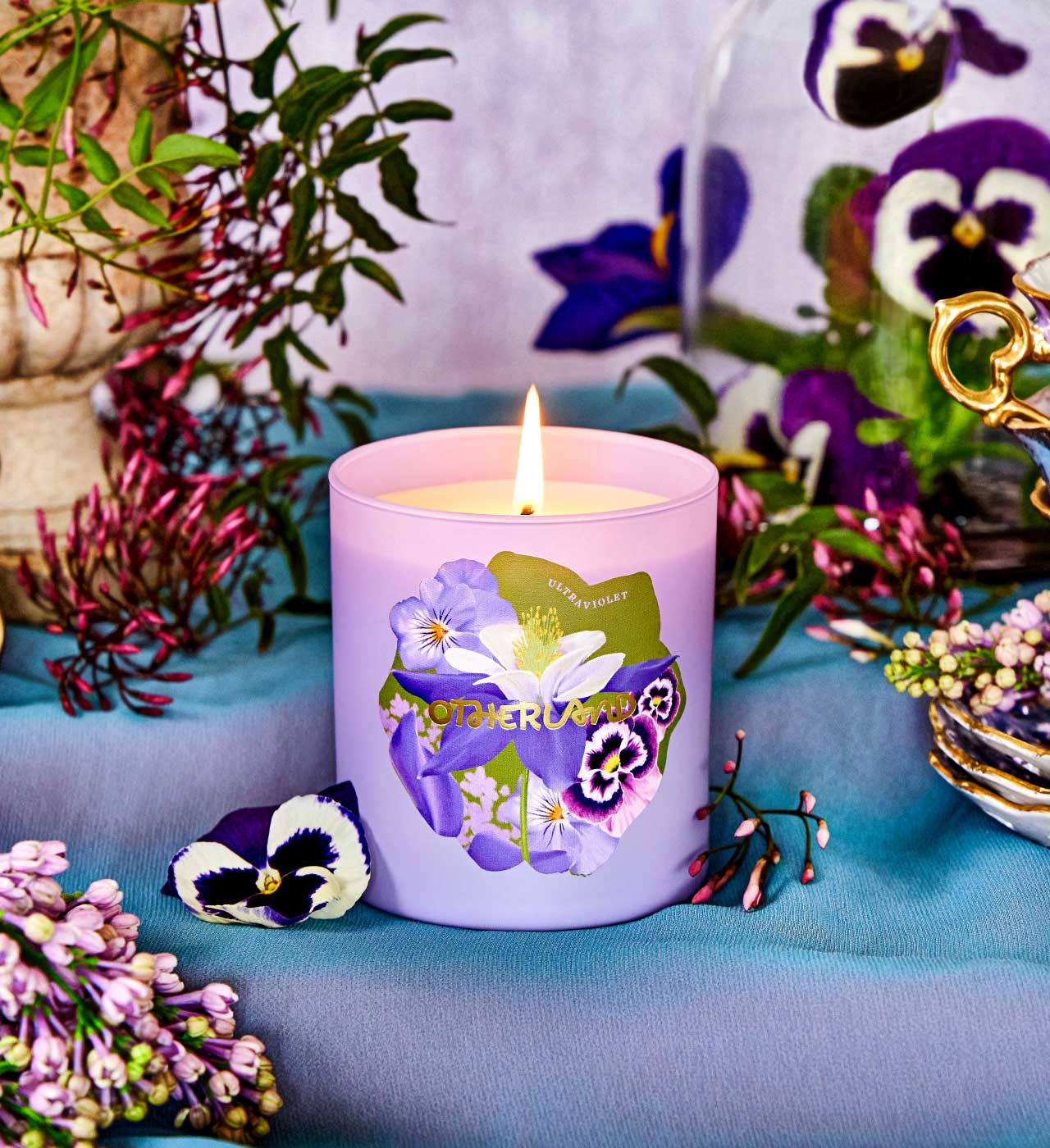 Purple candle with floral design on a table with flowers and plants - View 2