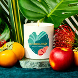 Candle with 'Otherland' branding surrounded by fruits and leaves