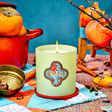 Candle with decorative label on a colorful tablecloth with pumpkins and cinnamon sticks.