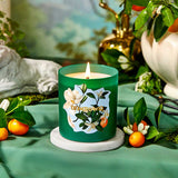 Green candle with floral design on a table with fruits and plants