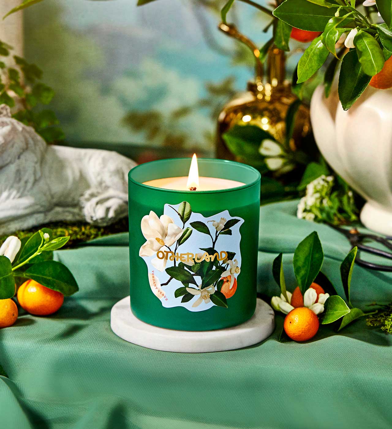 Green candle with floral design on a table with fruits and plants - View 2
